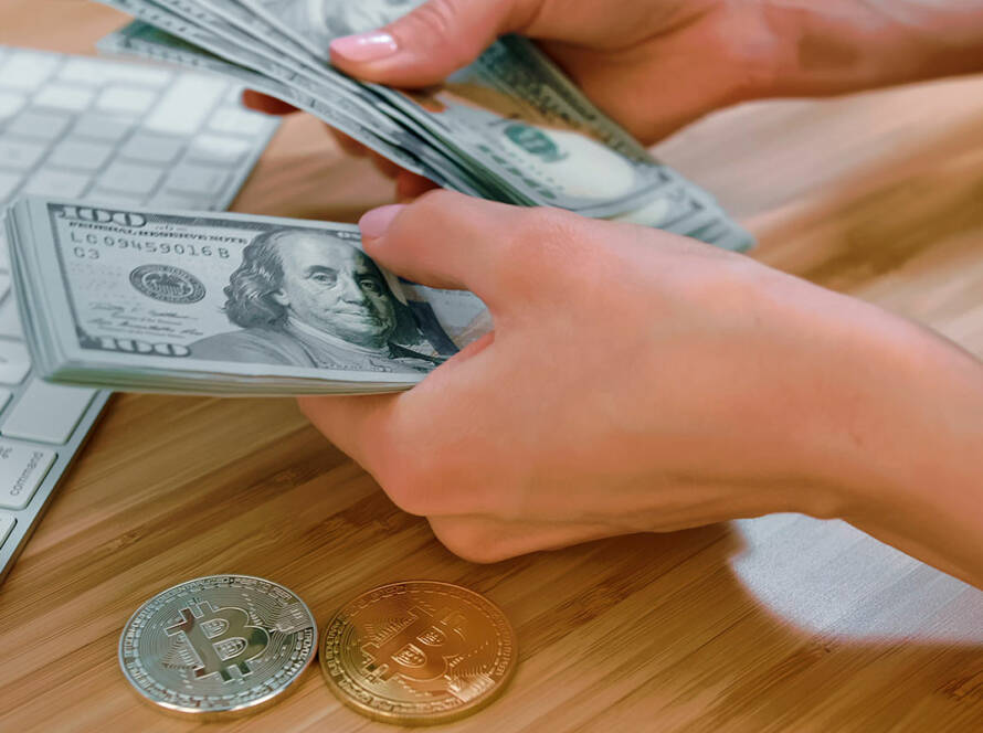 Person counting money near modern keyboard with bitcoins on desk near the money being counted.